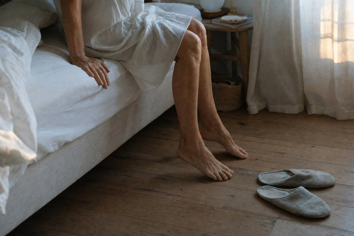 Bare feet about to touch the floor beside the bed at dawn